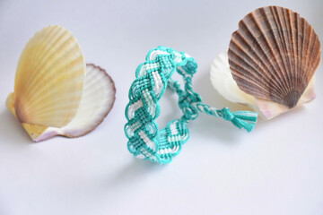 Selective focus of tied bright friendship bracelet Pigtail handmade of embroidery threads of marine and blue color on background with scallop seashells from the Japanese sea. Fresh and sea mood