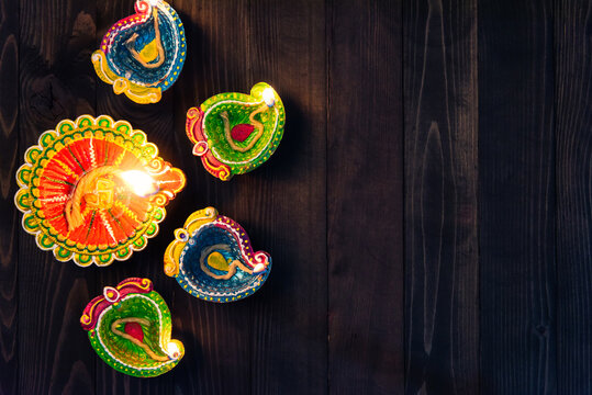 Top view overhead clay lit light a fire already on Diya or oil lamp, studio shot on black wooden background, Decoration of Hinduism rangoli, Happy celebration Deepavali or Diwali festival concept