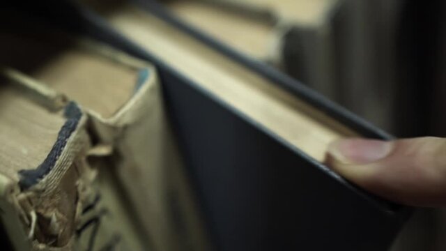 Clean index finger of caucasian thin man with a clean fingernail slides on palettes of books and searches for the necessary literature, chooses a textbook and pulls volume  two fingers off the shelf