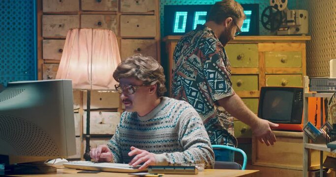 Caucasian funny man wih mustache, computer programist nerd in glasses working at vintage PC monitor. Vintage style room of 70's. Male on background having troubles with old broken TV. Retro men.