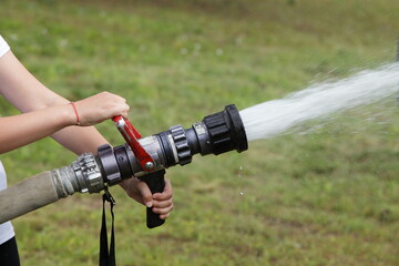 Boy scout pours water a powerful fire hose close up on summer day, children emergency training