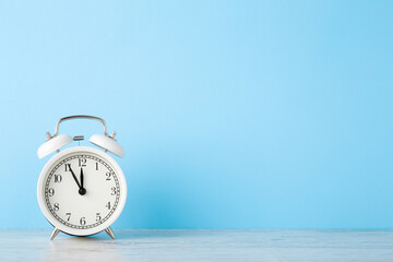 White alarm clock on wooden table at light blue wall background. Pastel color. Time concept....