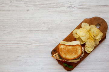 Homemade Pesto Chicken Sandwich with Potato Chips on a rustic wooden board on a white wooden background, top view. Flat lay, from above, overhead.