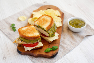 Homemade Pesto Chicken Sandwich with Potato Chips on a rustic wooden board, side view. Close-up.