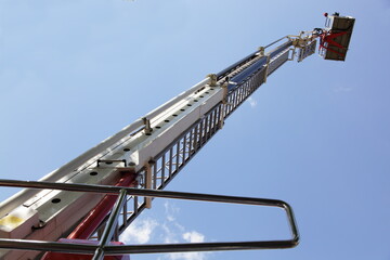 Tall extendable fire ladder close up in perspective on blue sky background, firefighter rescue...