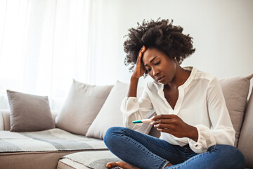 Sad Young Woman With Pregnancy Test At Home. Disappointed african-american girl getting unexpected result from pregnancy test. Woman desperate after reading pregnancy test result