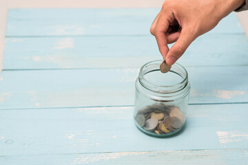 Hand putting Coins in glass jar with blank empty label for giving and donation money concept