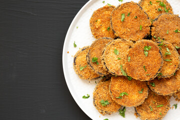 Homemade Garlic Parmesan Baked Eggplant on a plate on a black background, overhead view. Flat lay, top view, from above. Copy space.