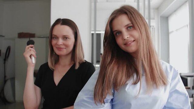 Confident caucasian adult makeup artist with young pupil in beauty studio, they posing at camera, after master class, share experience.