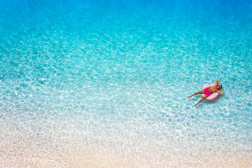 A man in swimsuit floats on a donut shaped inflatable over turquoise, clear sea nexto to the beach...