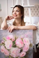 A woman artist holds a picture on an easel at home. The painter paints oil paintings.