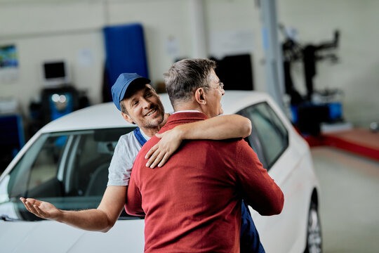 Happy auto repairman and his customer embracing while greeting in a workshop.