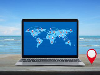 Map pin location button with connection line and world map on modern laptop computer on wooden table over tropical sea and blue sky with white clouds, Map pointer navigation online concept, Elements o