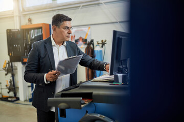 Mid adult manager working on a computer in auto repair shop.