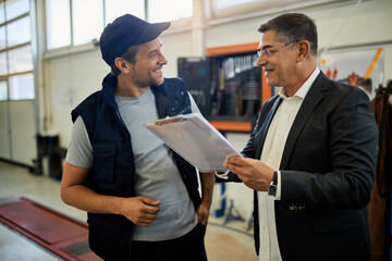 Happy auto repairman and his manager going through reports in a workshop.