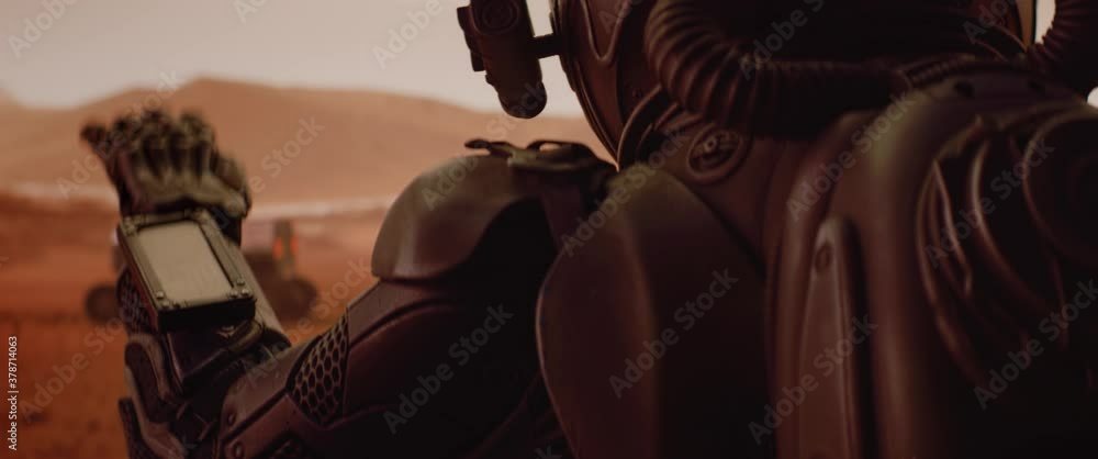 Wall mural handheld tracking back view of astronaut wearing space suit walking on a surface of a red planet. ma