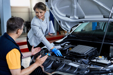 Female manager and auto mechanic examining car engine in auto repair shop.