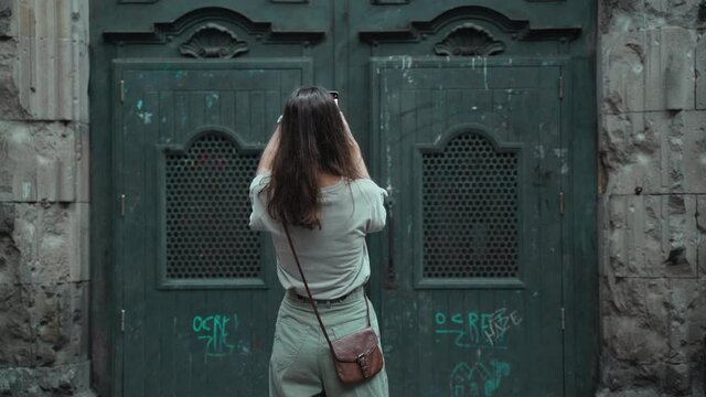 Beautiful long-haired brunette making photo of a large carved door. Young attractive woman taking pictures of stunning buildings. Pretty tourist makes selfie in a beautiful city.Mobile phone.