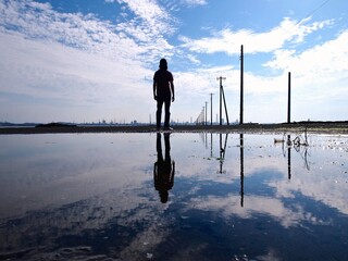 電柱のある海で遠くを眺めている人と水面に映るリフレクション