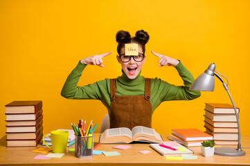 Photo of amazed high school girl sit table do materials home work point index finger sticker paper...