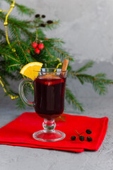 Hot mulled wine with cinnamon, anise, cloves and orange in a mug on the background of a Christmas tree.
