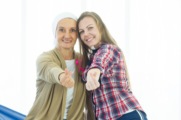A young woman and a senior breast cancer patient showing a hand symbolizing mini heart shape, smile...