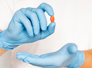 Hands doctor's in medical gloves hold a red pill. Blue disposable gloves isolated on a white background. Pharmaceutical concept. medicine, research concept