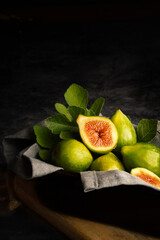 Still life of basket of whole figs with one open. Decorated with napkin and leaves. Dark background
