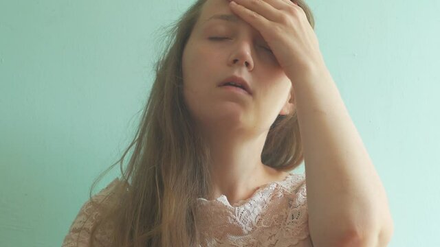 Stressed brown hair woman with headache on pastel mint background. Tired young lady without make-up feel pain, massaging temples. Hard to wake up, morning concept. PMS premenstrual syndrome problems.