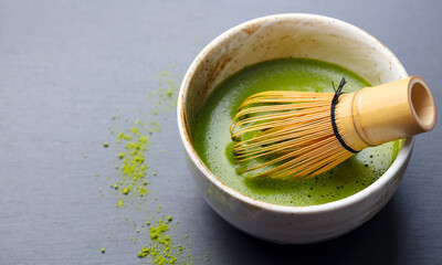 Matcha green tea cooking process in a bowl with bamboo whisk. Grey background. Copy space. Close up.