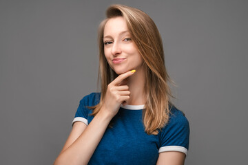 Photo of attractive female in casual blue t shirt making up plan in mind. Studio shot, gray background