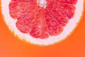 Slice of half red grapefruit on orange background, juicy citrus section texture. Abstract summer wallpaper, bright tropical pattern. Healthy food concept.
