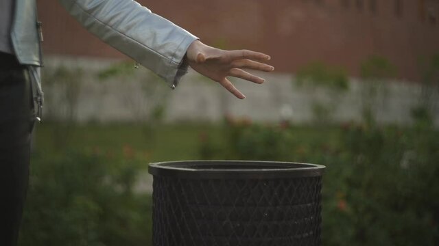 Girl metal jacket park center city holds her hand empty cup coffee colorful patterns on trash can street. Throws used mug into trash can. Environmental protection. Bio technology. Waste sorting.