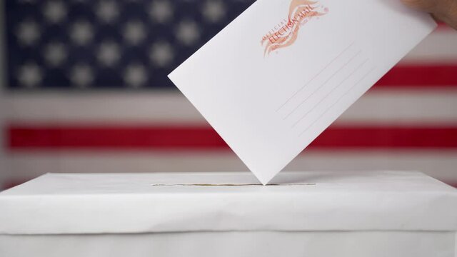 Maski, India 14 September, 2020 : Concept of Absentee Ballot Mail in voting at US election - Close up of hands dropping mail inside the ballot box with us flag as background