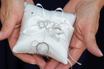 Two wedding rings on small white cushion in bride marriage hands