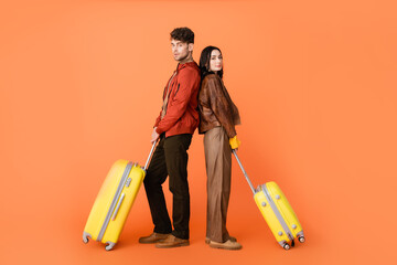 full length of trendy couple in autumn outfit standing back to back with yellow baggage on orange