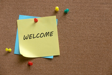 A colorful push pins and memo notes written with Welcome on a cork board.