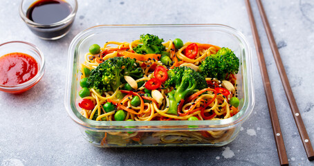 Stir fry noodles, udon with vegetables in lunch box. Grey background. Close up.