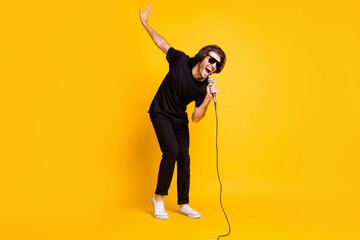 Full length photo of young man hold mic sing open mouth raise hand wear black t-shirt pants white...