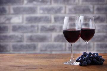 Glass of red wine and grape. Stone wall background. Wooden table. Close up.