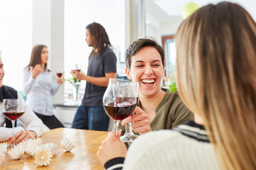 Lachende Frau trinkt Wein mit Freundin bei Party in Küche