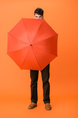 full length of man in brown pants holding umbrella on orange