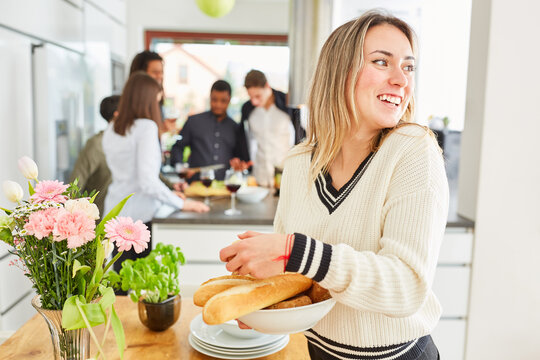 Frau beim Tisch decken mit Baguette in Küche vor Freunden