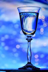 Glass of sparkling wine of champagne against the background of a winter fairy-tale landscape. Glittering lights and reflection in a glass of fir trees in the snow. Christmas background concept.