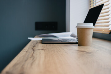 Fototapeta premium Laptop stands on a wooden table, workplace at home with a Cup of coffee. Work from home with a view from the window