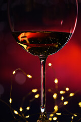 Glass with red wine and garland lights on a dark burgundy background. An atmosphere of privacy and intimacy.