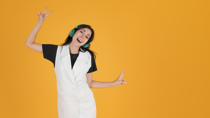 Image of a happy young woman listening to music with earphones. Portrait of a cheerful caucasian girl wearing wireless headphones and dancing on yellow background with copy space.
