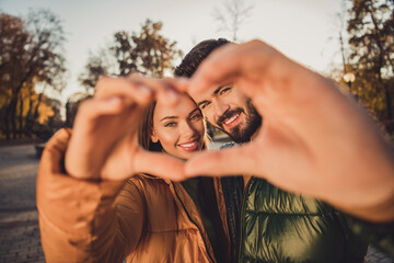Portrait of charming affectionate couple make fingers heart in fall town center park relax wear...