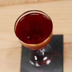 Elysian Cocktail in Nick & Nora gold rimmed glass on wood table with plant in background with a deep red color from the top