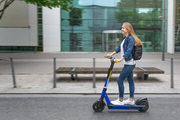 Urban city lifestyle. Young beautiful woman riding an electric scooter in downtown district. Modern urban background.